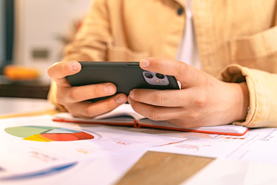 A business person checking their phone while working with graphs and charts on a desk.