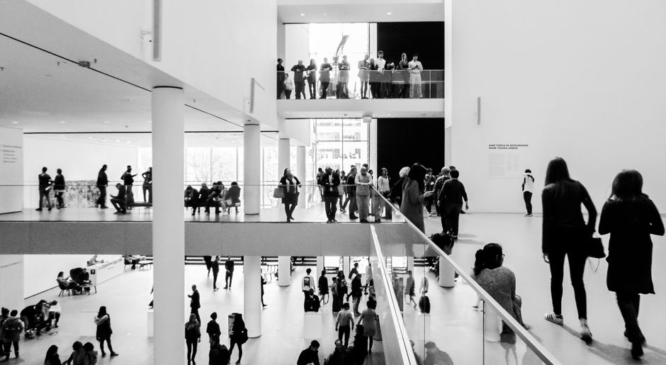 A dynamic black and white image of people in a modern museum setting.