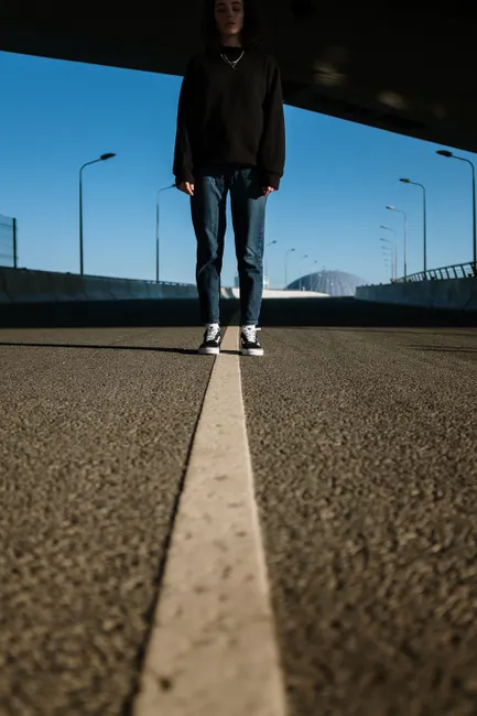 A lone individual stands on an empty divided road under a clear blue sky, emphasizing isolation.