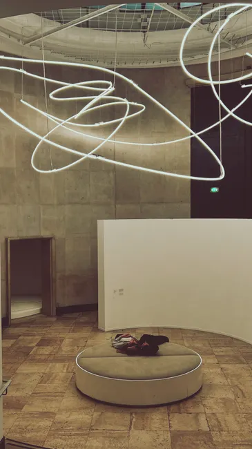 A visitor rests under dynamic lighting in a modern Paris art gallery.