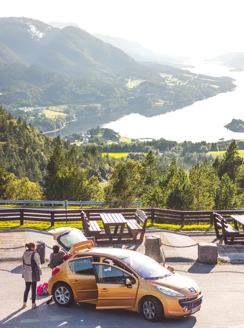 Breathtaking view of Norway's mountains with travelers and a car at a roadside stop.