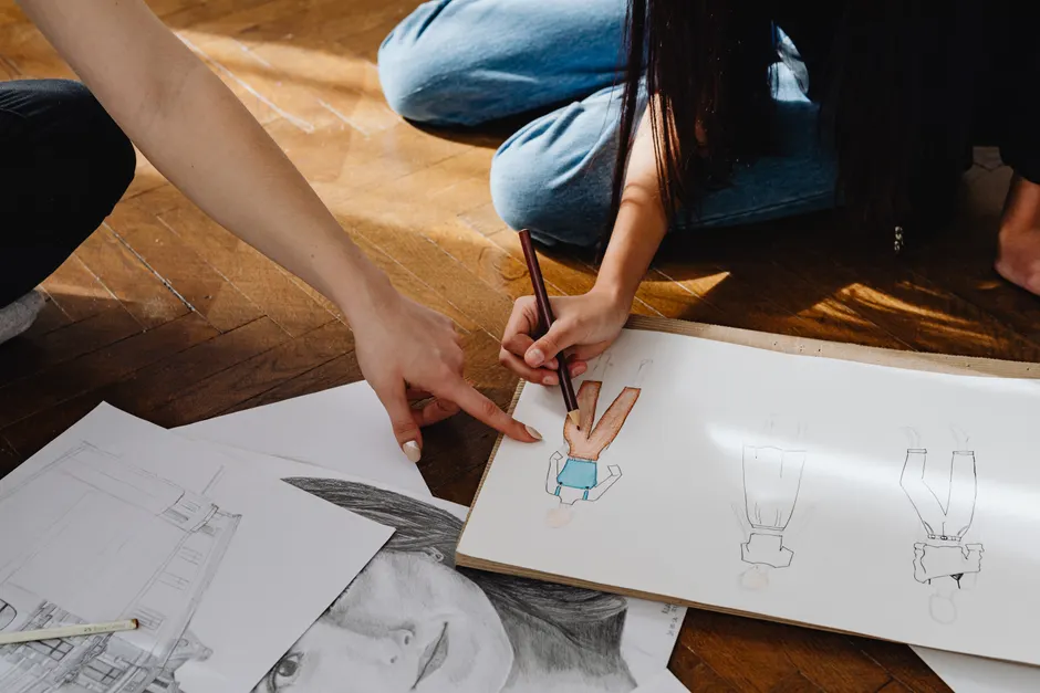 Close-up of hands sketching fashion designs on paper indoors.