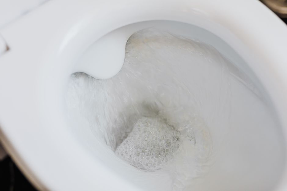 High angle of clean white ceramic toilet bowl with flushing foamy water in bathroom