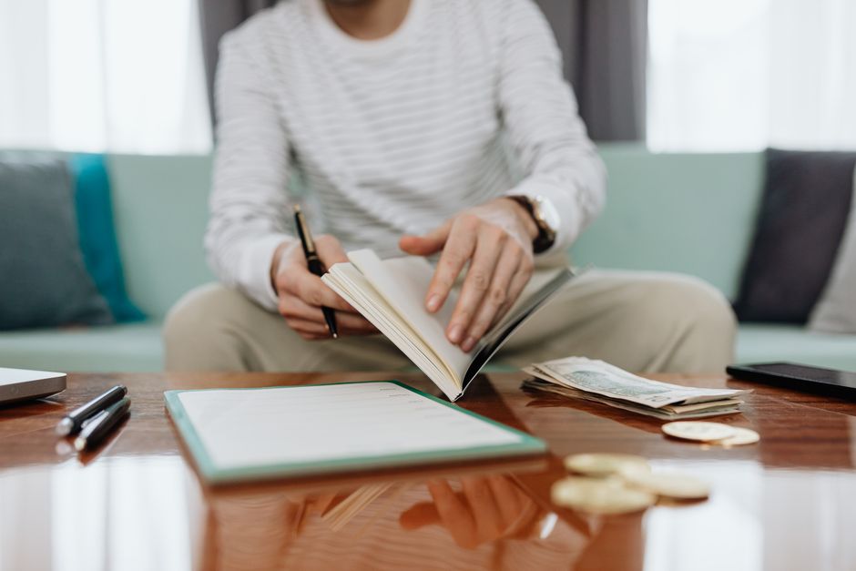 Individual reviewing finances at a table with notebook, money, and laptop.