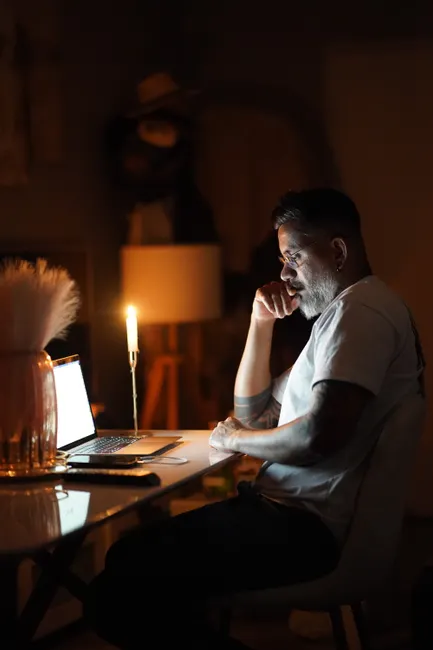 Man focused on laptop work at home office with candlelight, capturing evening's reflections.