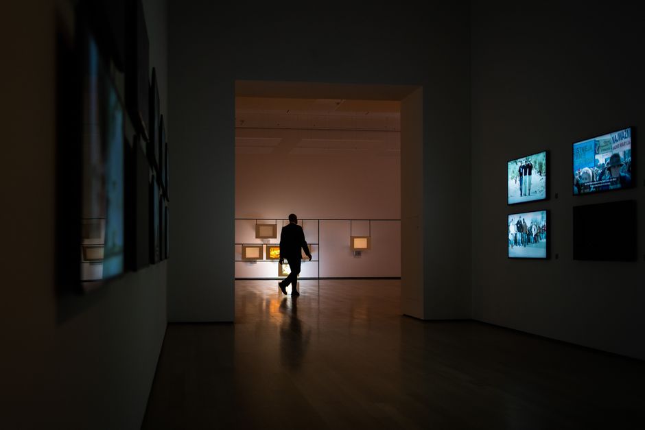 Silhouette of a man walking through a dimly lit art gallery surrounded by illuminated screens.