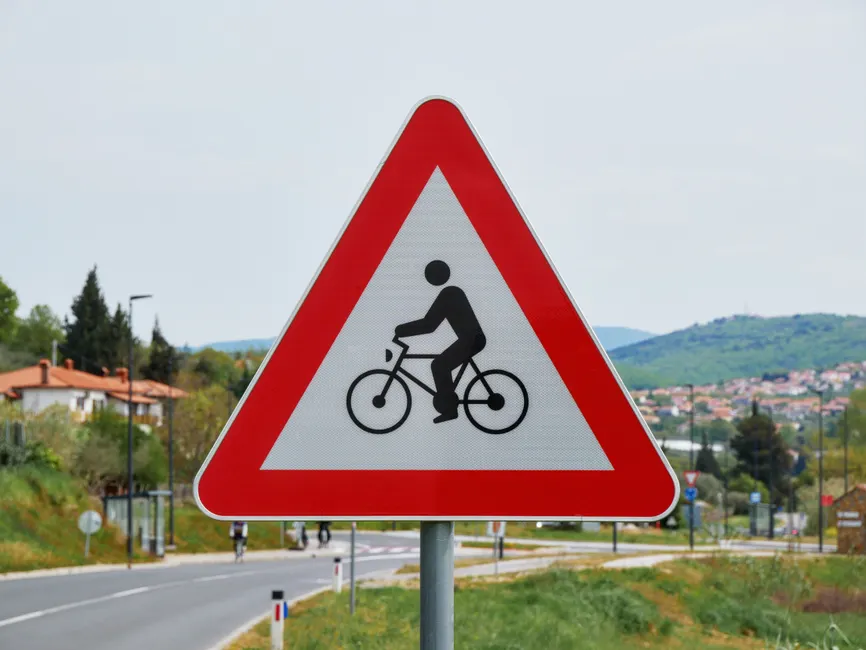 Triangular bicycle warning sign along a rural road indicating cyclist presence.
