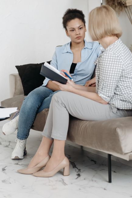 Two women engaging in a thoughtful conversation in a contemporary office setting.