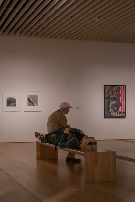 Visitors resting on a bench in a modern art gallery, surrounded by paintings and atmosphere.