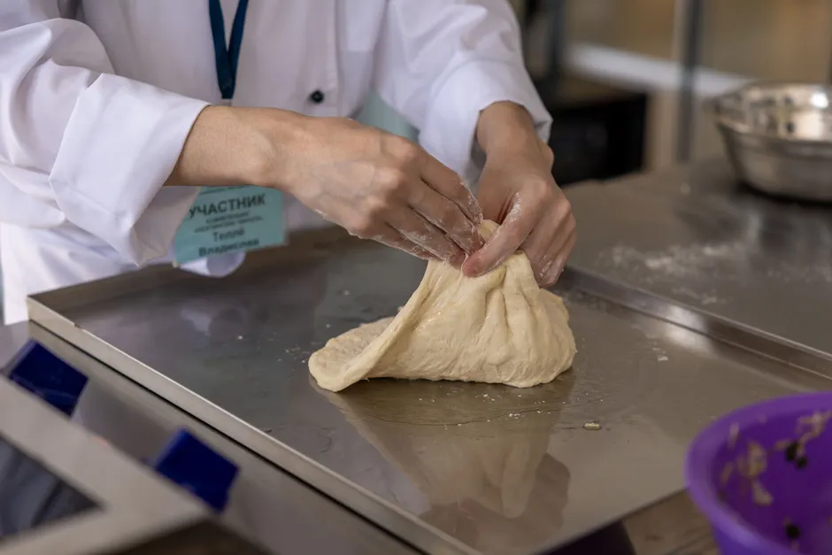 A chef skillfully kneads dough on a metal surface in a modern culinary setting.