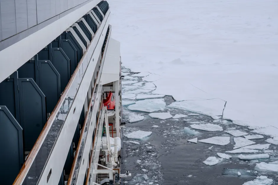 A cruise ship navigates through ice in the Arctic, showcasing icy waters and frozen landscapes.