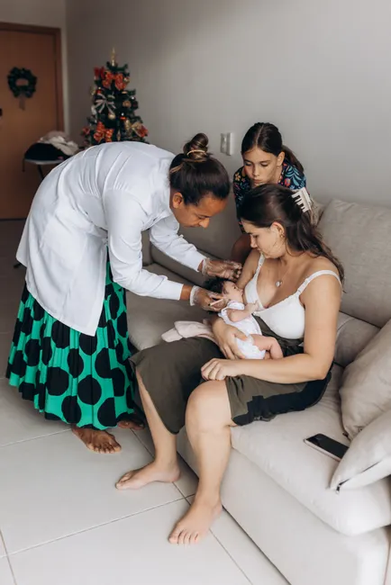 A doctor visits a family at home, checking a newborn baby with mother and child present.