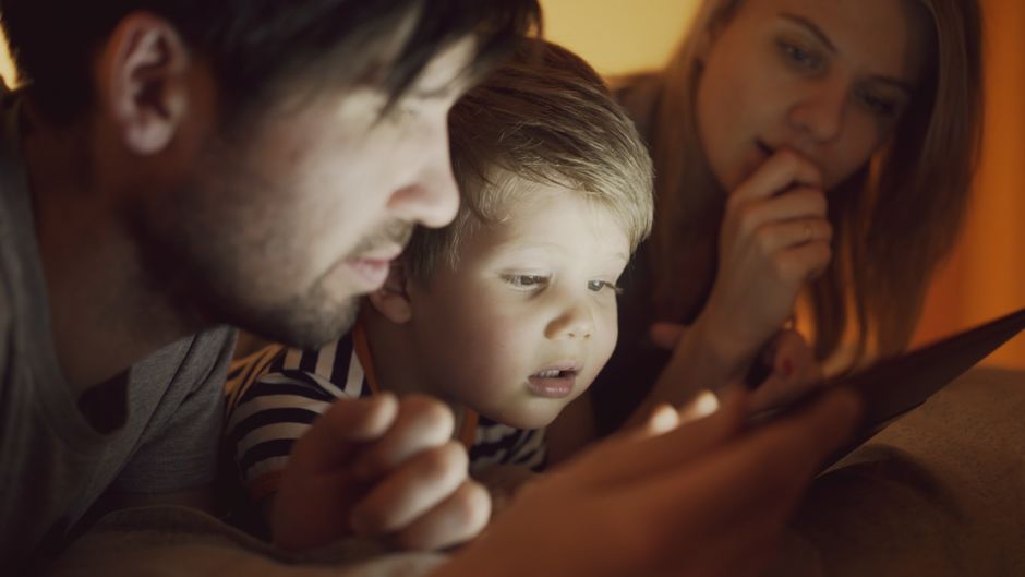 A family of three, including parents and a child, intently watching a digital tablet together indoors.
