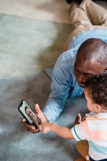 A father and his young child interact joyfully during a video call, showcasing family bonding indoors.