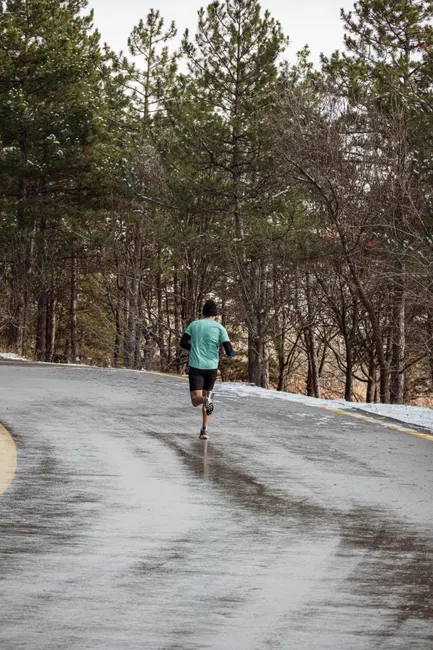 A lone runner in a green shirt jogs on a wet forest road in Ankara, Türkiye.