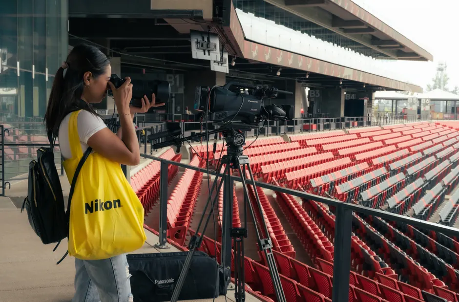 A woman photographer captures images in an empty stadium using professional camera equipment.