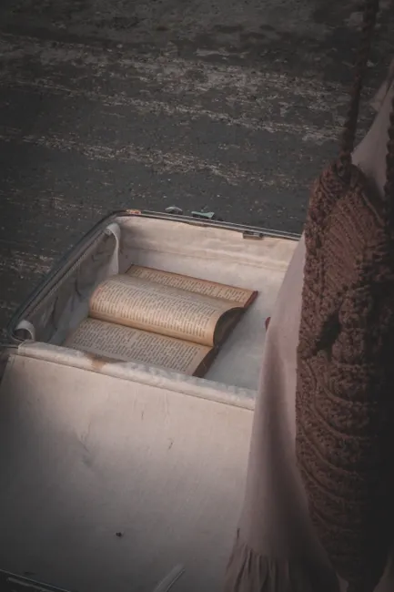 An open book inside a vintage suitcase on a textured floor, conveying a sense of travel and nostalgia.