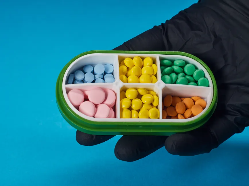 Colorful pills in a four-compartment box held by a gloved hand on a blue background.