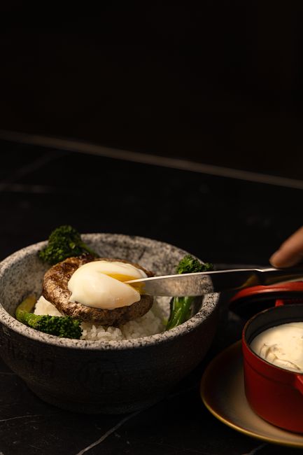 Delicious gourmet rice bowl topped with steak, poached egg, and broccoli, captured in a moody setting.