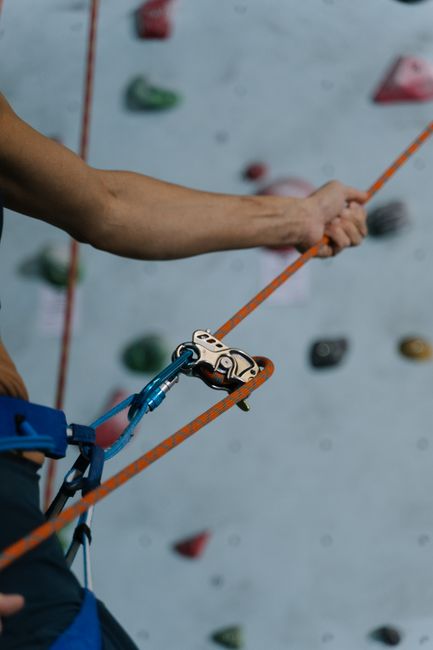 Detailed close-up of a climber securing a rope with a belay device at an indoor climbing gym.
