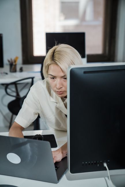 Focused office worker with blonde hair working diligently at a computer desk in modern office.