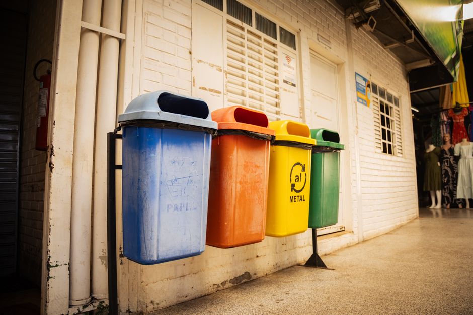 Four recycling bins for different materials in a market setting, emphasizing waste sorting and environmental awareness.