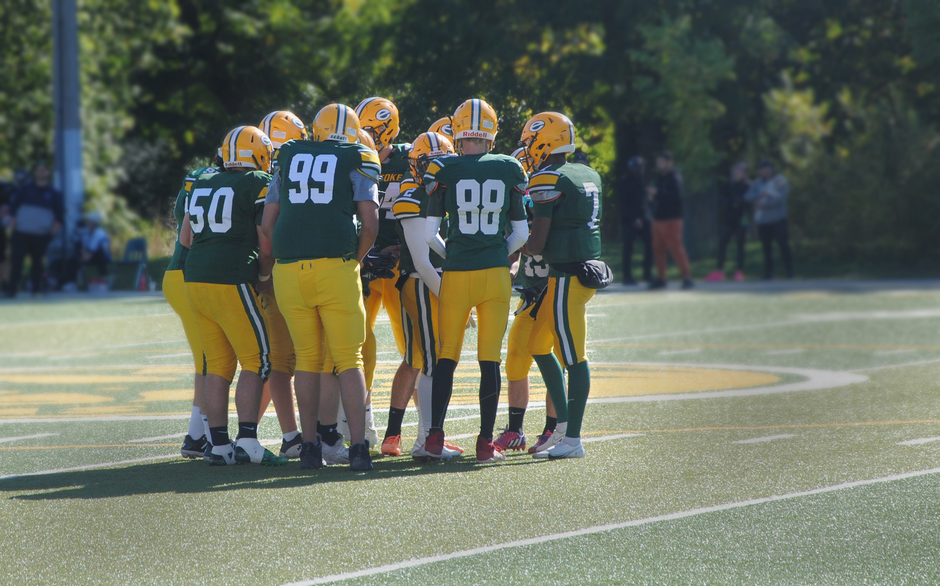 Group of football players in uniform huddling on an outdoor field, preparing for play.