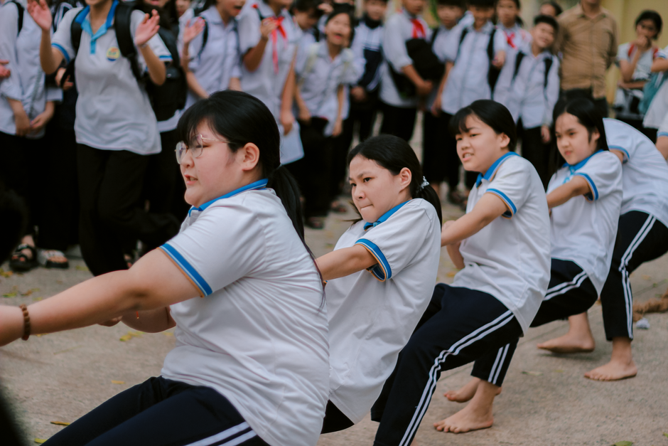Group of students in uniform engaged in a lively tug of war competition outdoors.