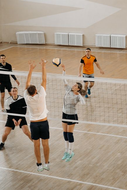 Men and women athletes competing fiercely in an indoor volleyball match with dynamic action on the court.