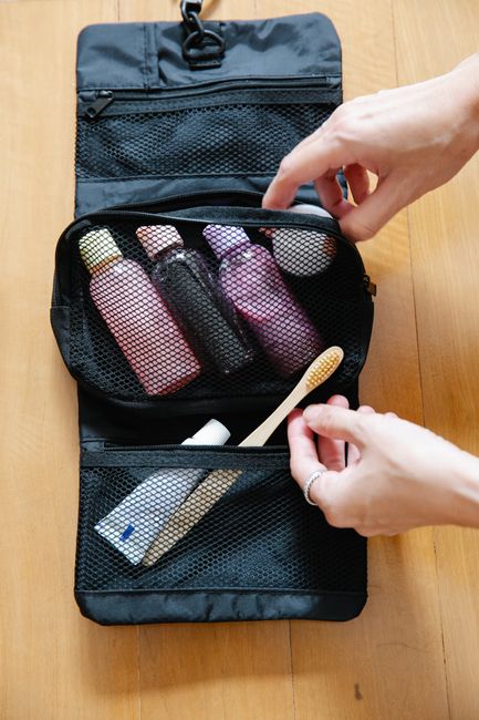 Open toiletry bag with bottles and a bamboo toothbrush on wooden surface.