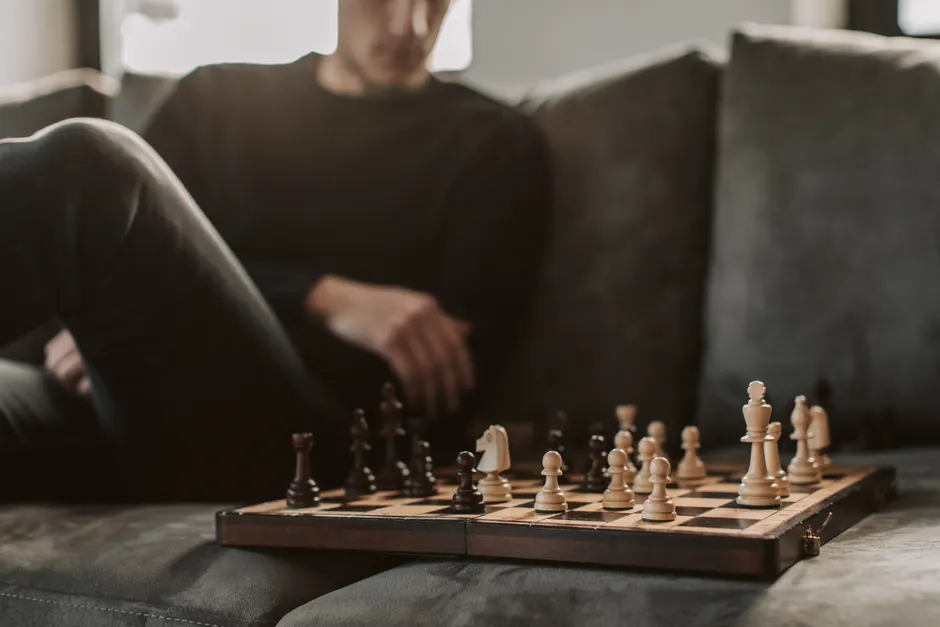 Person relaxing with a chessboard on a couch. Strategic focus and casual ambiance.