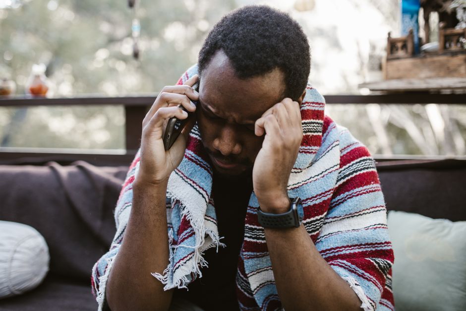 Thoughtful adult man having a conversation on the phone while wrapped in a cozy blanket outdoors.