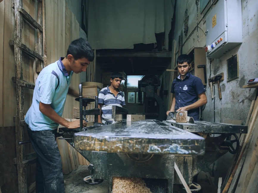 Three young men engaged in carpentry work inside a traditional woodworking workshop.