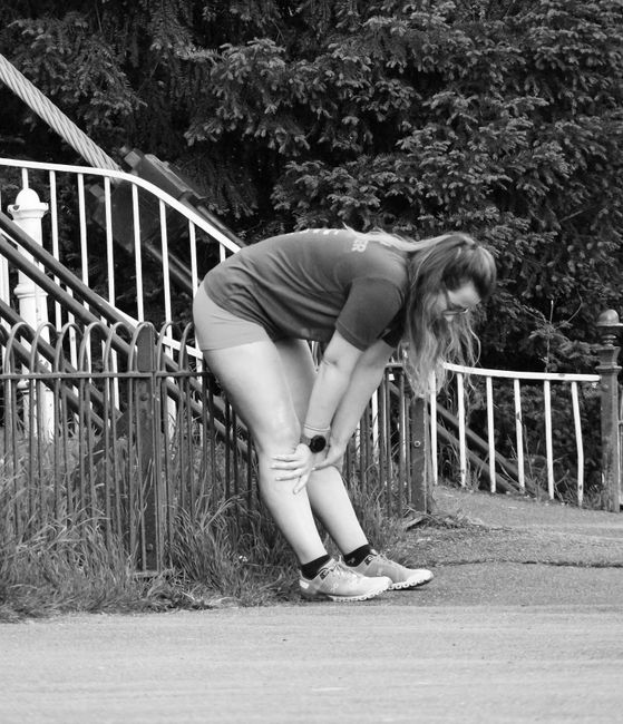 Tired female runner catching her breath leaning on a fence in a park.