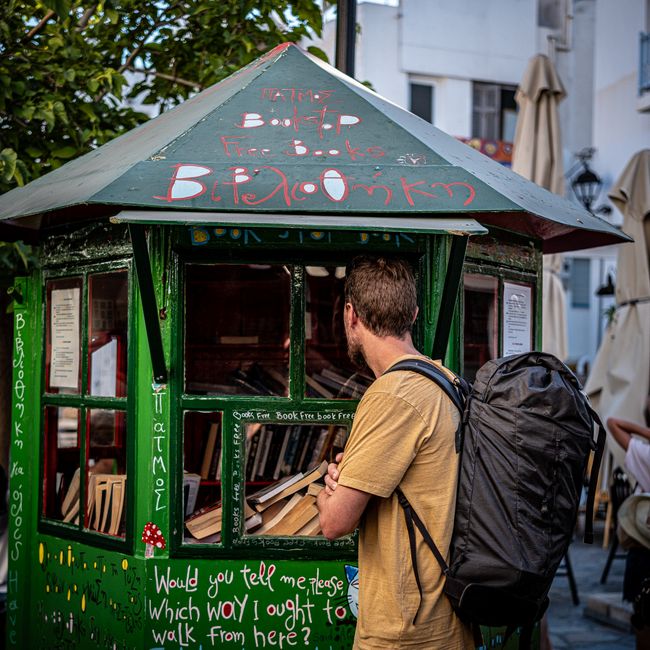 Traveler browsing a free book kiosk in Greece. Outdoor reading spot.