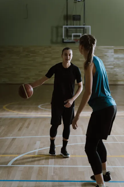 Two women engaging in a basketball game on an indoor court, focused on practice.