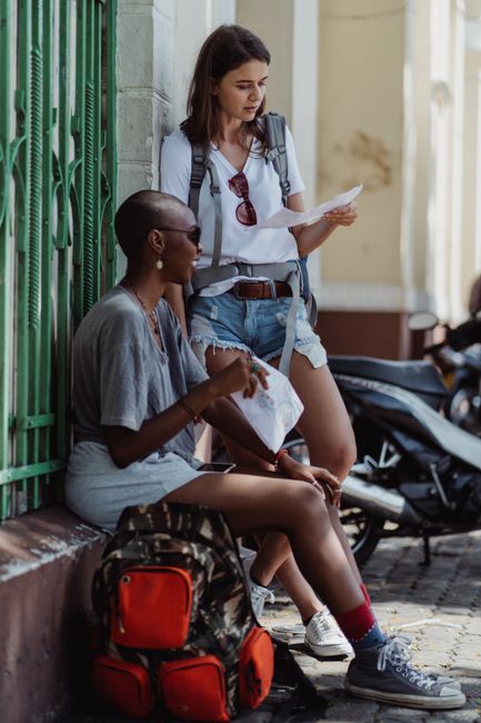 Two women travelers checking a map outdoors, exploring a city street.