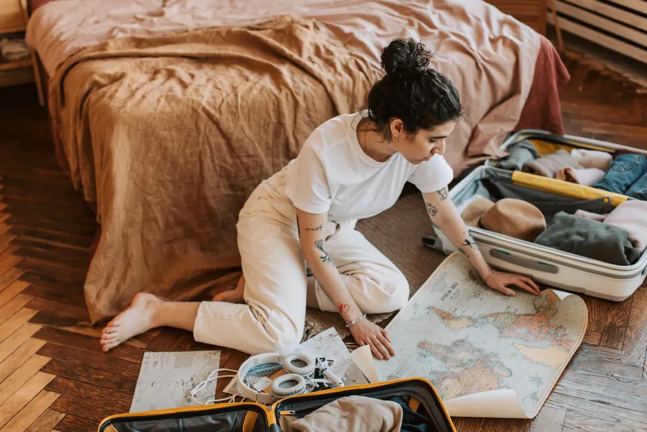 Young woman planning a travel route indoors, surrounded by luggage and a map.