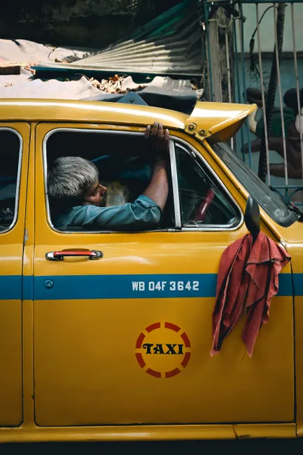 A classic yellow taxi with a resting driver in Kolkata, India, showcasing daily life.