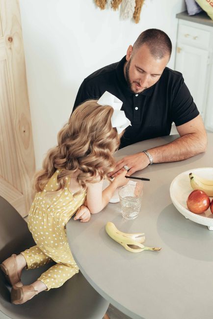 A father and daughter engaging in drawing activities at the kitchen table with fruits nearby.