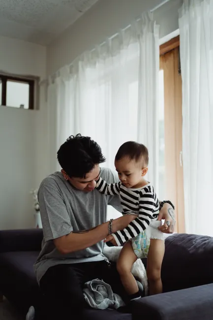 A father lovingly changes his son's diaper at home, showcasing family bonding and care.