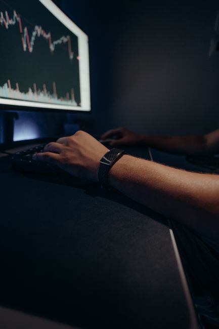A person working late at night analyzing stock market data on a computer screen.