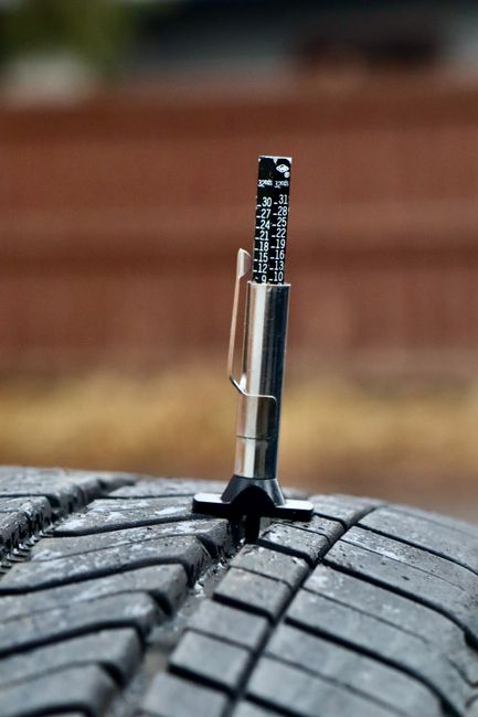Close-up of a tire tread depth gauge in a tire illustrating measurement accuracy.