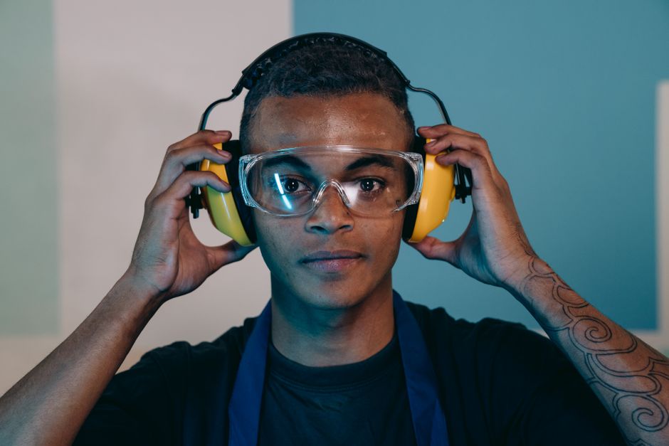 Close-up portrait of a young male engineer wearing safety glasses and earmuffs in an industrial setting.