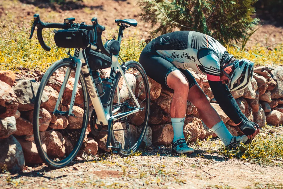 Cyclist pauses to stretch during a ride on a rocky path surrounded by nature in Türkiye.