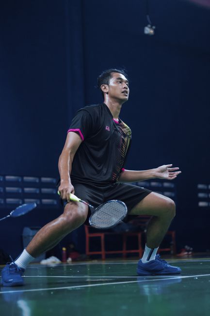 Male badminton player shows skillful stance on indoor court. Captured mid-action.