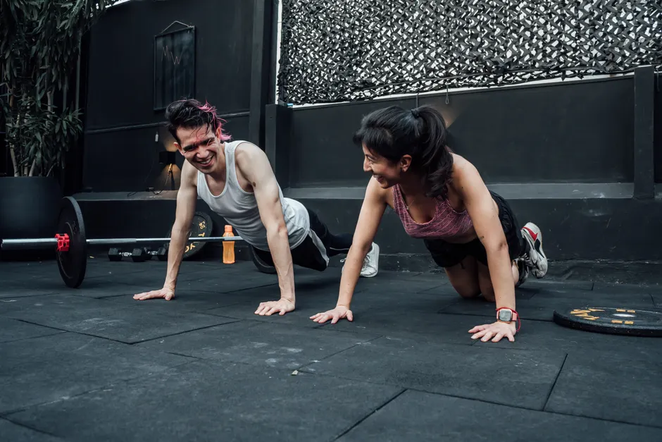 Man and woman doing pushups while smiling during a workout inside a Mexico City gym.
