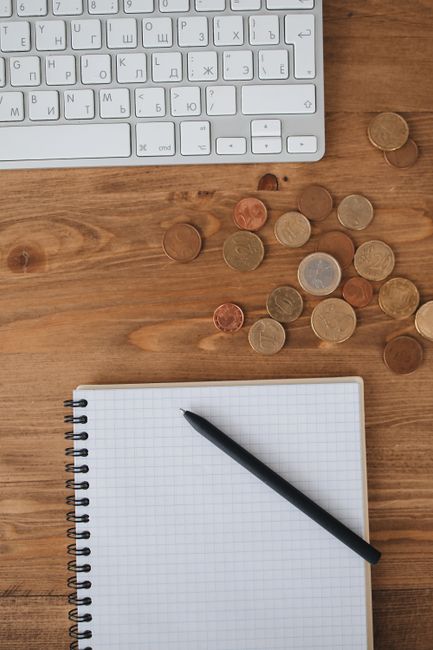 Overhead view of a workspace with keyboard, coins, and a notebook on a wooden desk