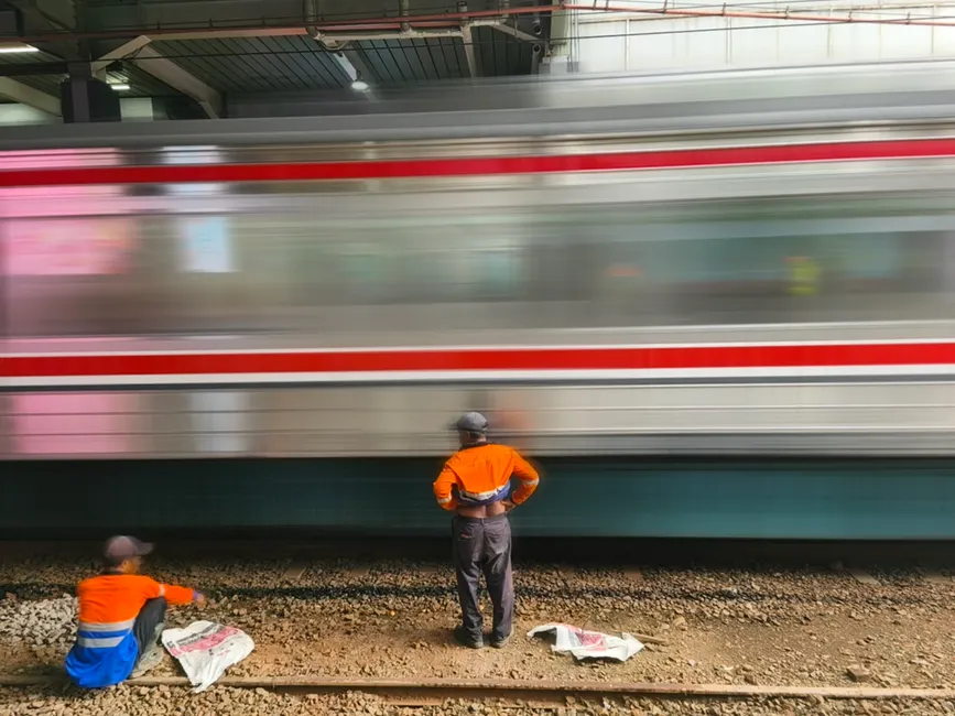 Railway workers in Jakarta watch a speeding commuter train passing through a station.